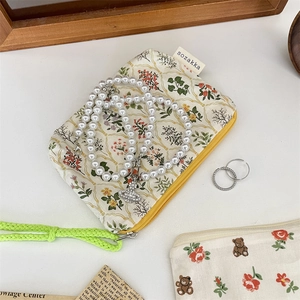 Close-up of a floral patterned storage pouch with pearl necklace and silver rings