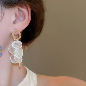 Close-up of golden textured hoop earrings with cascading white shell-like round tassels