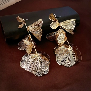Macro detail of gold layered petal earrings with long metallic wire tassels