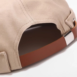 Detail of adjustable brown leather strap and silver metal buckle on a khaki docker cap