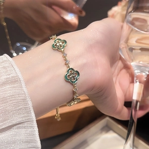 Détail d'un bracelet trèfle doré avec émail vert et zircons sur le poignet d'un modèle