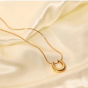 Macro detail of gold U-shaped horseshoe pendant with snake chain on silk fabric