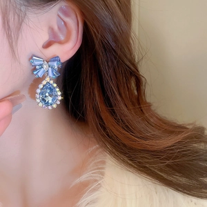 Close-up of blue crystal teardrop earrings with a bow design worn by a female model