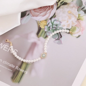 Detail of 18K gold bracelet featuring white pearls and a zircon geometric charm