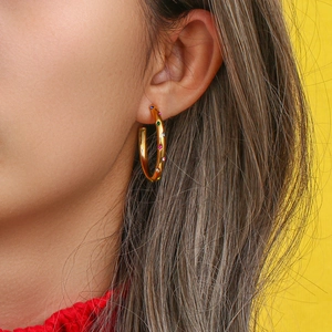 Macro side view of golden stainless steel hoop earrings with colorful zircon inlay