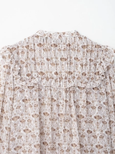 Détail d'une blouse en mousseline fleurie avec imprimé botanique or et volants plissés