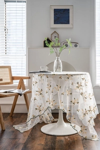 Detailed close-up of white mesh tablecloth with yellow floral embroidery and scalloped edges