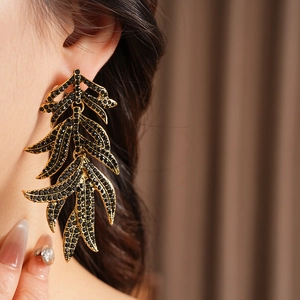 Close-up of vintage gold leaf earrings with black rhinestones on a model's ear