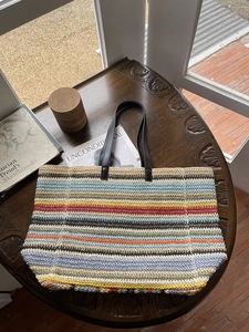 Multicolor striped woven straw tote bag with black leather handles on a vintage wood table