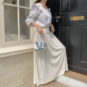 Detail of silver sequin handbag with chain strap shown against a modern street backdrop
