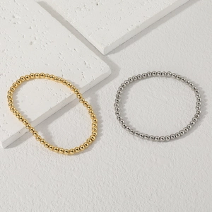 Dettaglio di braccialetti minimalisti con perline oro e argento su una pietra bianca venata