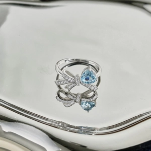 Macro shot of silver ring with blue heart zircon and ribbon detail on mirror surface