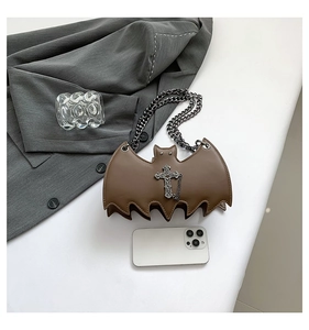 Brown bat-shaped mini chain bag with silver cross detail next to a smartphone