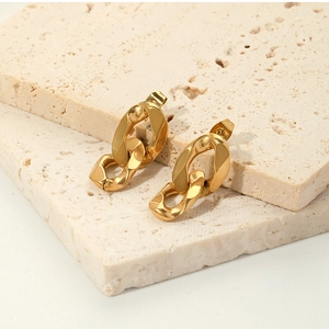 Close-up of gold 18K geometric chain earrings on a natural stone display pedestal