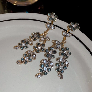 Macro view of gold floral drop earrings with sparkling green and white gemstones