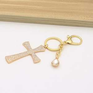 Close-up of golden cross keychain pendant with sparkling rhinestones on white surface