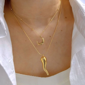 Layered gold necklaces with moon and horn pendants on a white shirt background