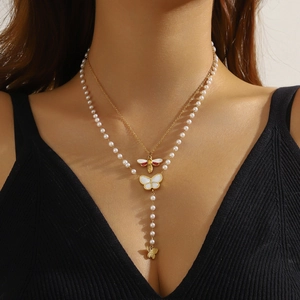 Double-layered gold chain necklace with pearl strand, bee and butterfly charms on model
