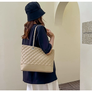 Détail du sac cabas beige matelassé avec bandoulière chaîne porté par un mannequin en décor épuré