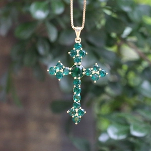 Detailed view of a gold cross pendant necklace featuring brilliant green zircon stones
