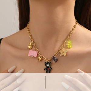 Close-up of gold chain necklace with colorful bear, flower, and heart charms on model