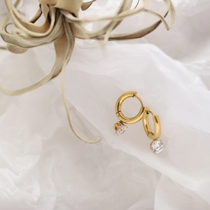 Macro detail of gold hoop earrings with sparkling cubic zirconia pendant on white paper