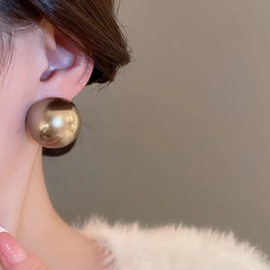Gros plan macro d'une boucle d'oreille sphérique dorée polie portée par un mannequin