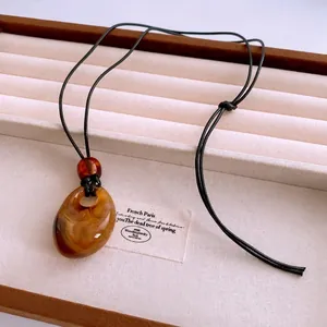 Vintage amber-tone acrylic teardrop pendant necklace on a minimalist black wax cord