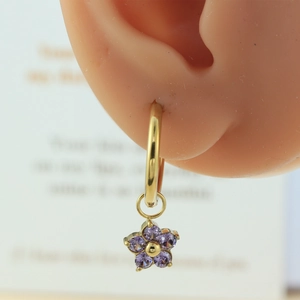 Close-up of golden hoop earrings with purple flower pendants on a model's ear