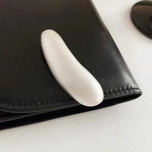 Close-up of minimalist white matte bean-shaped brooch pinned on black leather edge