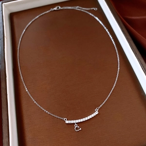 Close-up of silver chain necklace with zircon bar and C letter pendant on leather tray