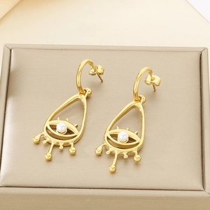 Détail de boucles d'oreilles œil maléfique dorées avec perle et design diamant en V