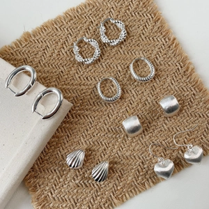 Minimalist silver geometric earrings set with shell and heart motifs on brown linen