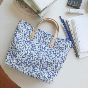 Detail of floral tote bag showing blue fabric, metal rivets, and leather handle grip