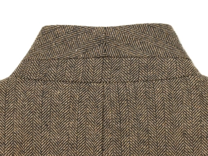 Detailed close-up of brown herringbone tweed fabric texture on a blazer collar