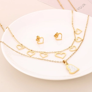 Close-up of golden double-layer heart necklace and earrings set on white plate