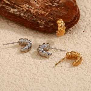 Detailed view of croissant style earrings in gold and silver finish on wooden block
