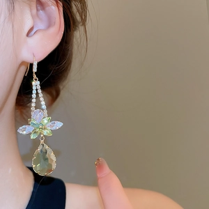 Close-up of elegant gold earrings with green flower accents and crystal teardrop pendants