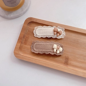 Close-up of two knit lace hair clips in beige and brown on a wooden tray with candle