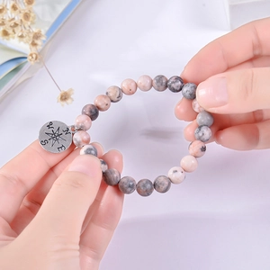 Close-up of natural stone bead bracelet featuring a silver compass pendant held in hand