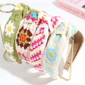 Detail view of colorful knitted floral headbands on a gold stand with daisy patterns