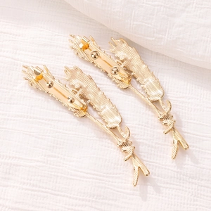 Detail of two gold-toned wheat ear hair clips with textured alloy on white fabric