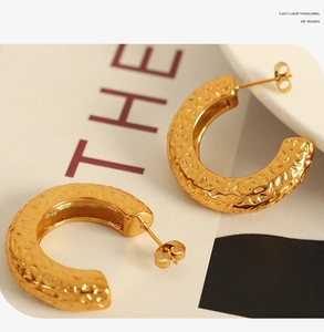 Detailed view of thick C-shape gold earrings featuring a handcrafted hammered metal texture