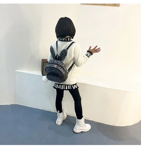 Girl wearing black sequin backpack with bunny ears and white plush ball charm accessory