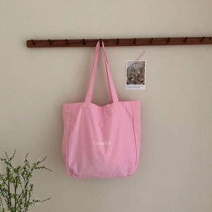Nahaufnahme der rosa Canvas-Einkaufstasche mit weißem Camellia-Schriftzug an der Wand