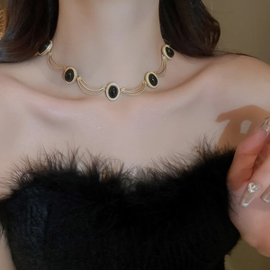 Close-up of a layered gold necklace with five black oval gemstones on a model's neck
