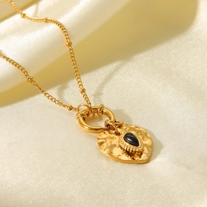 Close-up of hammered gold heart pendant with black gemstone on white silk fabric