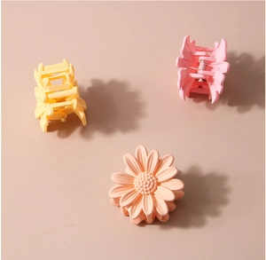 Close-up of three matte daisy hair clips in yellow, pink and apricot tones