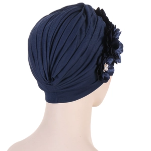 Dark blue pleated turban hat with three 3D flowers and pearl accents on white background