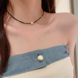 Détail du ras du cou avec perles noires et dorées et un pendentif en perle blanche